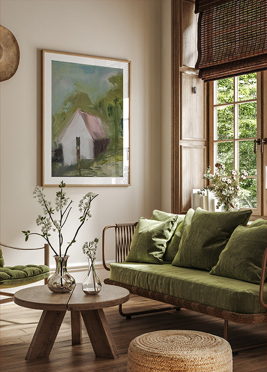 ein gemütliches Wohnzimmer mit einem großen Fenster, einem grünen Sofa, einem Couchtisch aus Holz und einem gerahmten Gemälde eines Hauses.